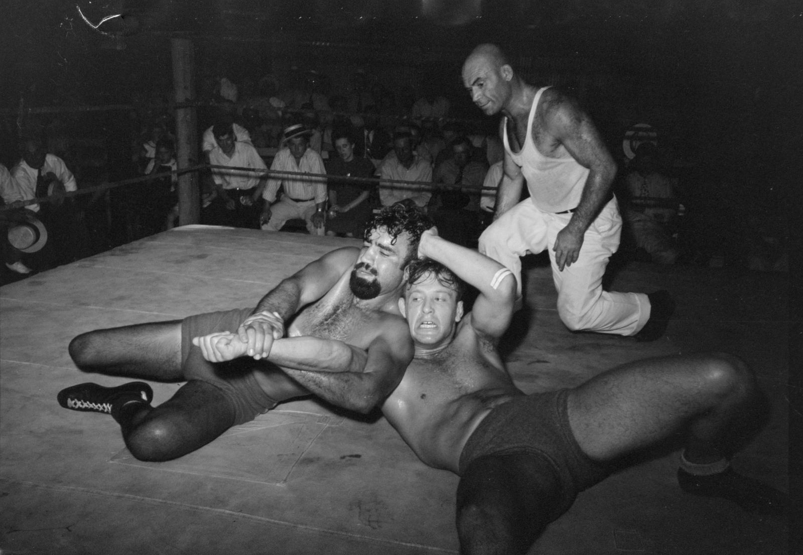 Two wrestlers grapple in an outdoor ring in Sikeston, Missouri, in 1938 while a referee watches